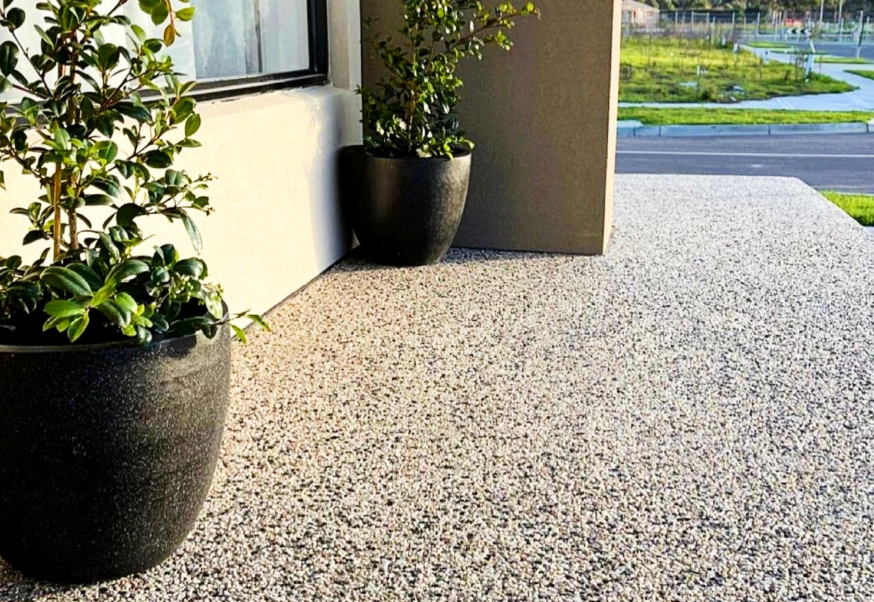 Two potted plants placed on top of an exposed aggregate ground outside a building.