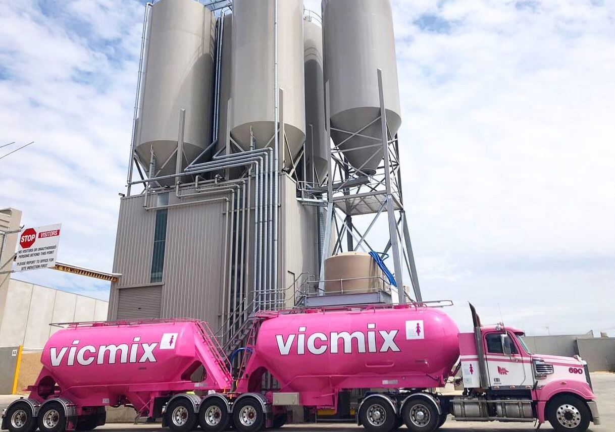 A pink Vicmix concrete mixer truck in a construction plant.