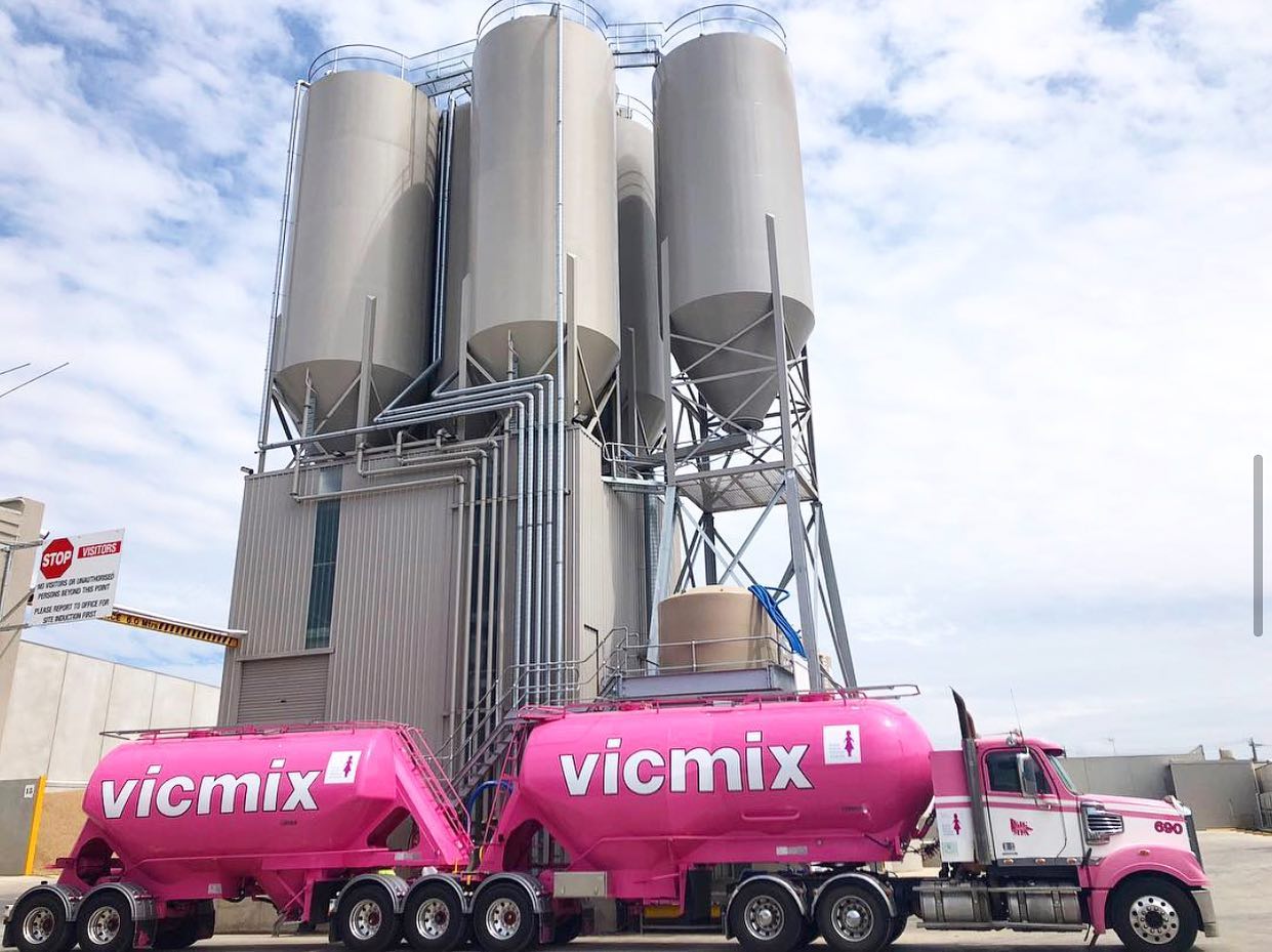 A pink Vicmix concrete mixer truck in a construction plant.